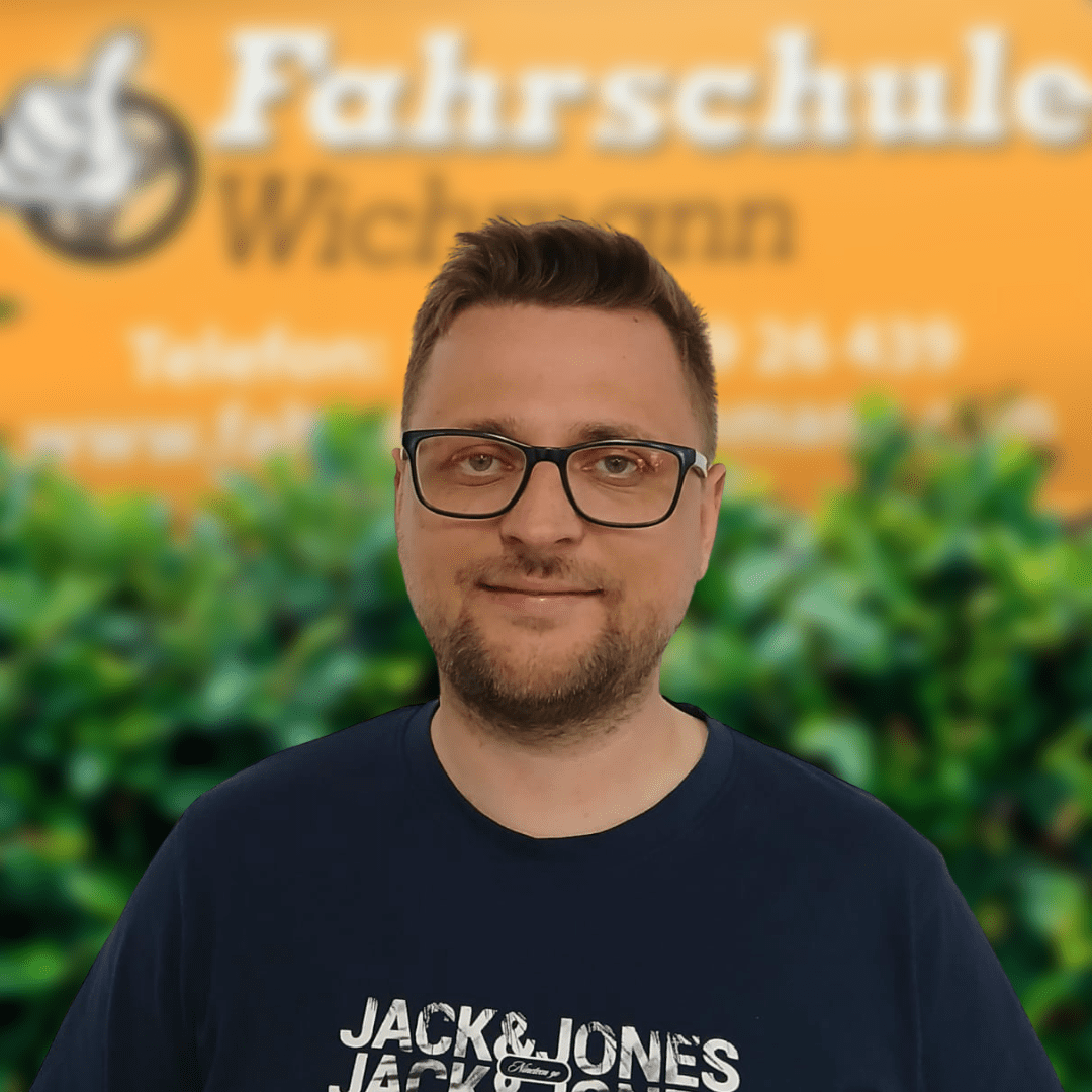 Mirco, Fahrlehrer der Fahrschule Wichmann in Oyten, Bassen und Borstel, begleitet Schüler kompetent auf dem Weg zum Auto-, Motorrad-, LKW- oder Anhängerführerschein sowie durch die Intensivfahrschule und Fahrlehrerausbildung. - Wichmann Fahrschule Oyten - Autoführerschein LKW Führerschein Motorradführerschein Mirco, Fahrlehrer der Fahrschule Wichmann, vor dem Firmenschild mit grünem Busch im Hintergrund.