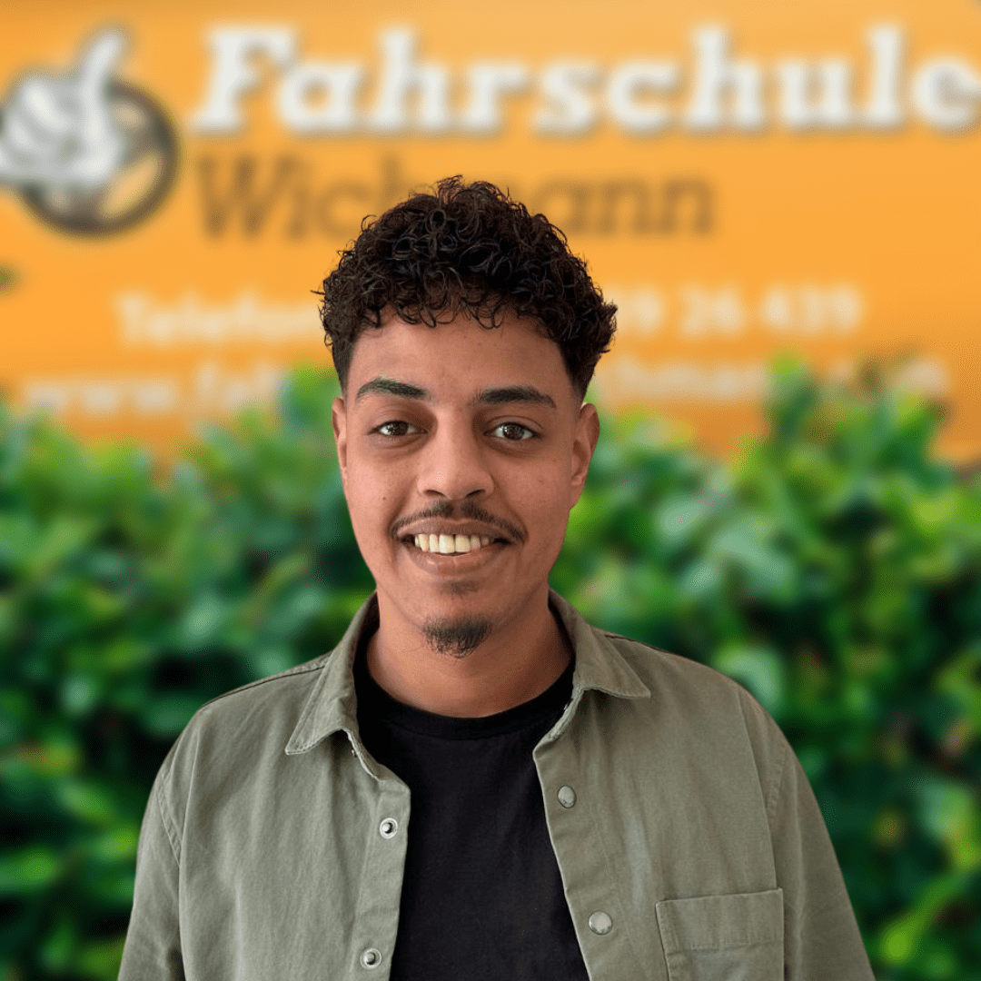 Sofiane, Fahrlehrer der Fahrschule Wichmann in Oyten, begleitet dich kompetent zum Auto-, Motorrad-, LKW- oder Anhängerführerschein – auch in Bassen und Borstel. Ideal für die Intensivfahrschule oder deine Fahrlehrerausbildung. - Wichmann Fahrschule Oyten - Autoführerschein LKW Führerschein Motorradführerschein Sofiane, Fahrlehrer der Fahrschule Wichmann in Oyten, steht lächelnd vor dem gelben Hintergrund der Fahrschule.