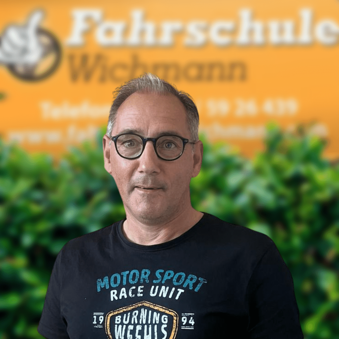 Thomas, Fahrlehrer der Fahrschule Wichmann in Oyten, begleitet Schüler aus Oyten, Bassen und Borstel kompetent zum Auto-, Motorrad-, LKW- oder Anhängerführerschein – inklusive Intensivfahrschule und Fahrlehrerausbildung. - Wichmann Fahrschule Oyten - Autoführerschein LKW Führerschein Motorradführerschein Fahrlehrer Thomas der Fahrschule Wichmann in Oyten vor dem gelben Firmenschild mit Logo und Kontaktinfos.