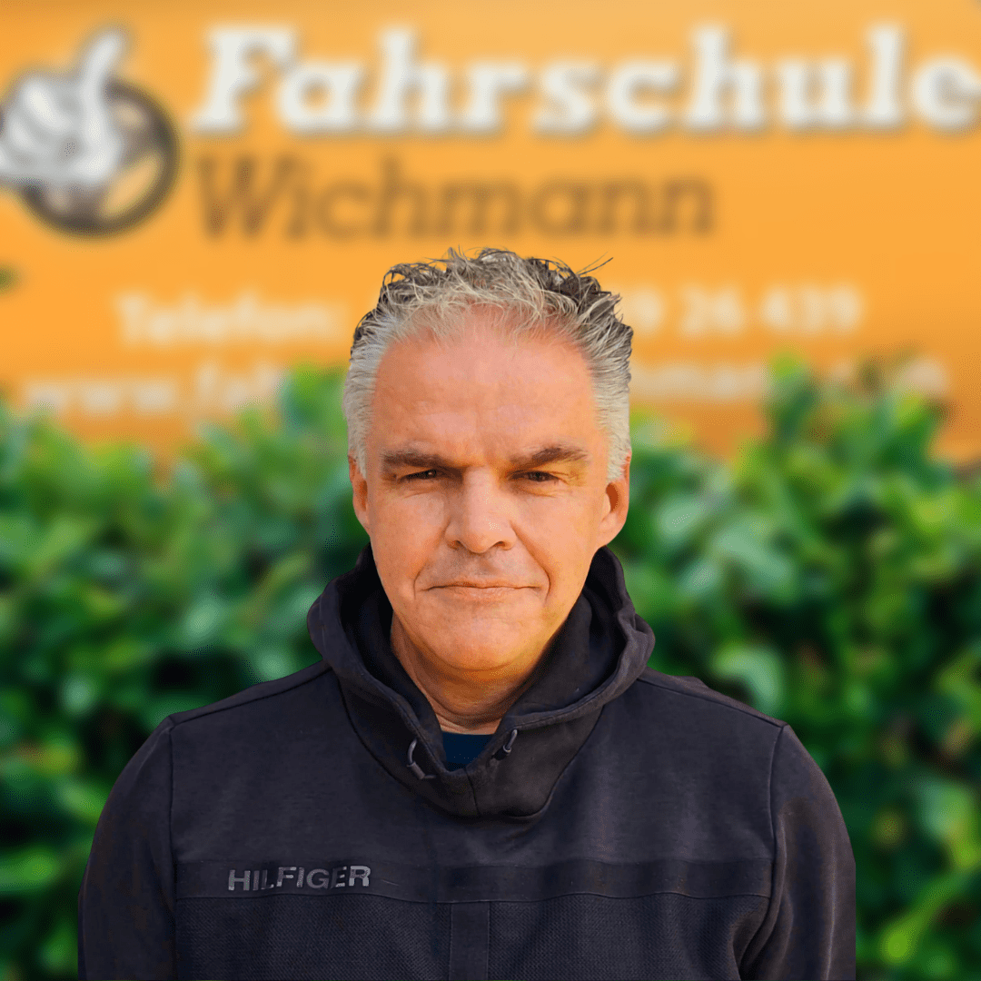 Thomas, Fahrlehrer der Fahrschule Wichmann in Oyten, Bassen und Borstel, spezialisiert auf Autoführerschein, Motorradführerschein, LKW- und Anhängerführerschein, Intensivfahrschule sowie Fahrlehrerausbildung, vor dem Schulgebäude. - Wichmann Fahrschule Oyten - Autoführerschein LKW Führerschein Motorradführerschein Thomas, Fahrlehrer der Fahrschule Wichmann, steht vor dem Schulgebäude in Oyten mit Logo im Hintergrund.